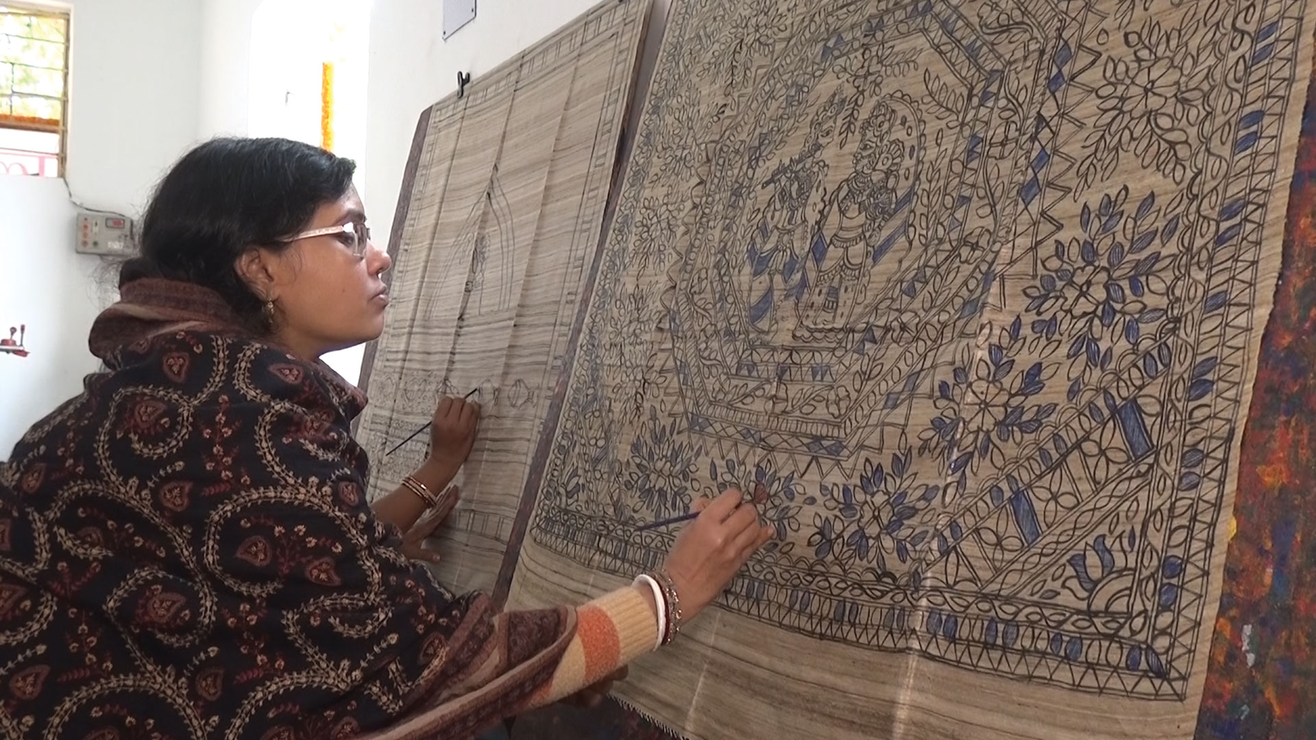 A woman painting madhubani designs into a fabric