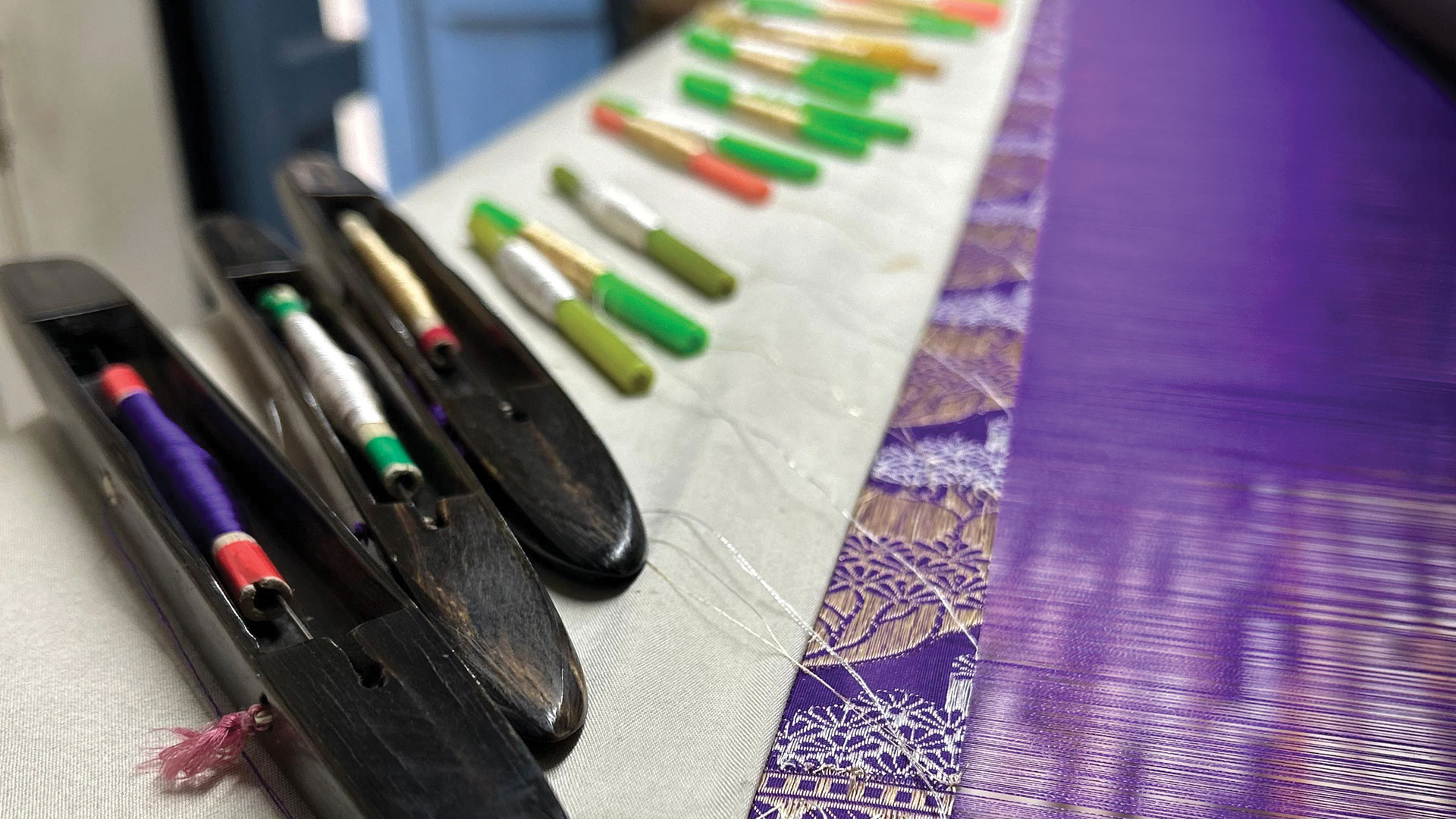 Two weavers threading gold threads into fabric with care